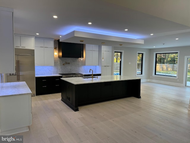 kitchen with appliances with stainless steel finishes, backsplash, a kitchen island with sink, sink, and light hardwood / wood-style floors