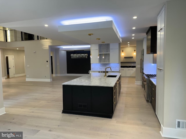 kitchen featuring sink, an island with sink, hanging light fixtures, and light hardwood / wood-style floors