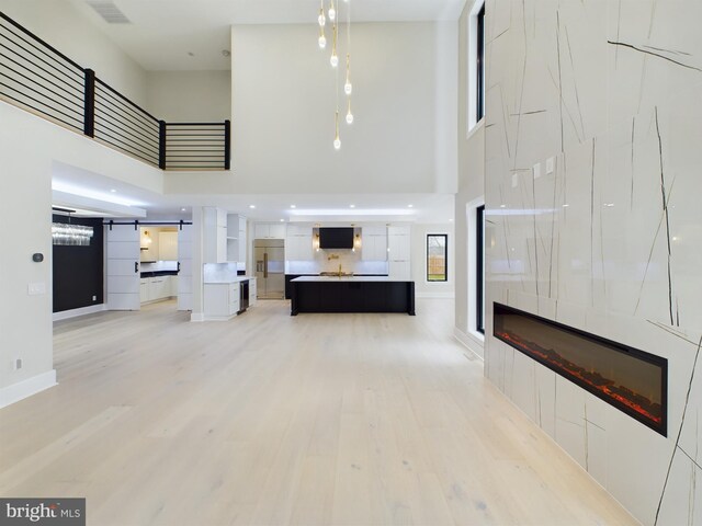 5005 Ravensworth Rd, Annandale, VA 22003 - unfurnished living room with a towering ceiling, a fireplace, light wood-type flooring, a barn door, and baseboards