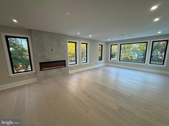 unfurnished living room featuring a high end fireplace, a wealth of natural light, and light hardwood / wood-style flooring