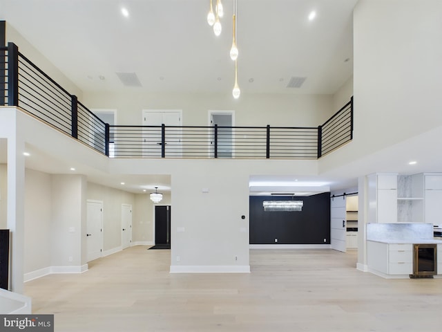 5005 Ravensworth Rd, Annandale, VA 22003 - unfurnished living room featuring wine cooler, a towering ceiling, light wood-type flooring, a barn door, and baseboards