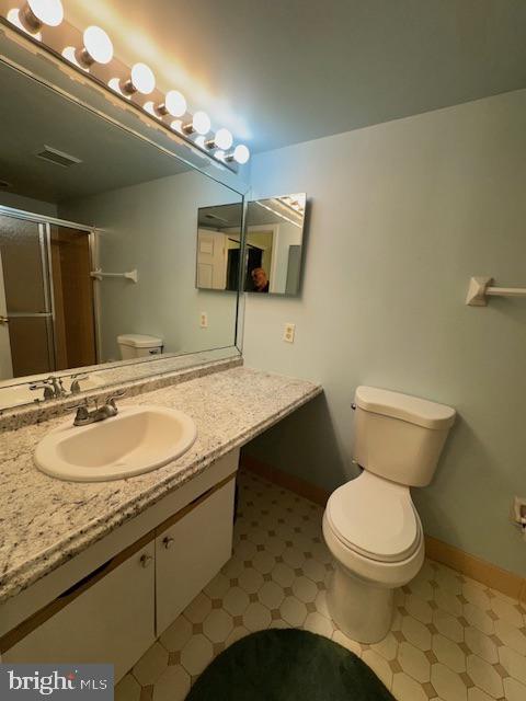 bathroom featuring toilet, vanity, and a shower with door