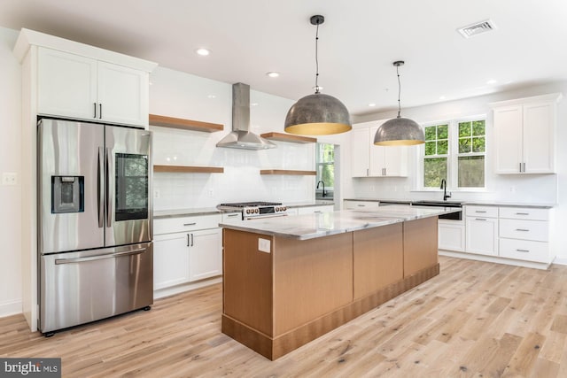 kitchen featuring wall chimney range hood, white cabinets, stainless steel appliances, and pendant lighting