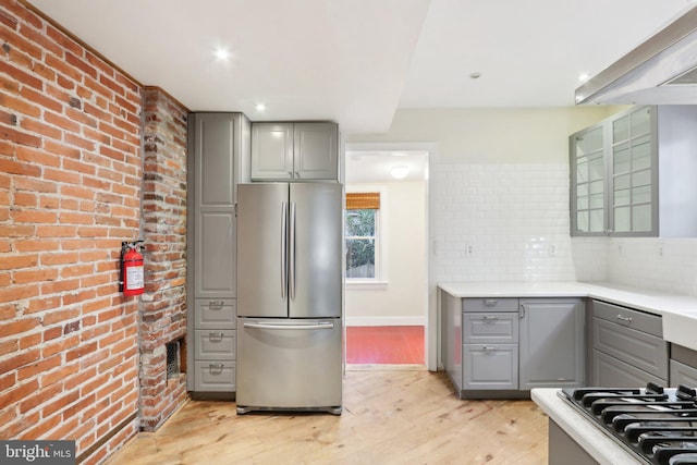 kitchen featuring gray cabinets, brick wall, appliances with stainless steel finishes, and light hardwood / wood-style floors