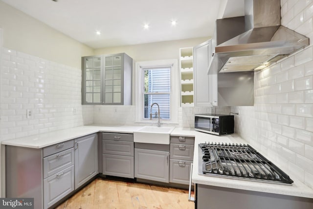 kitchen with sink, light hardwood / wood-style floors, wall chimney exhaust hood, gray cabinets, and decorative backsplash