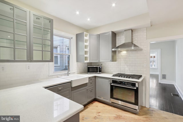 kitchen featuring a healthy amount of sunlight, stainless steel appliances, wall chimney exhaust hood, and sink