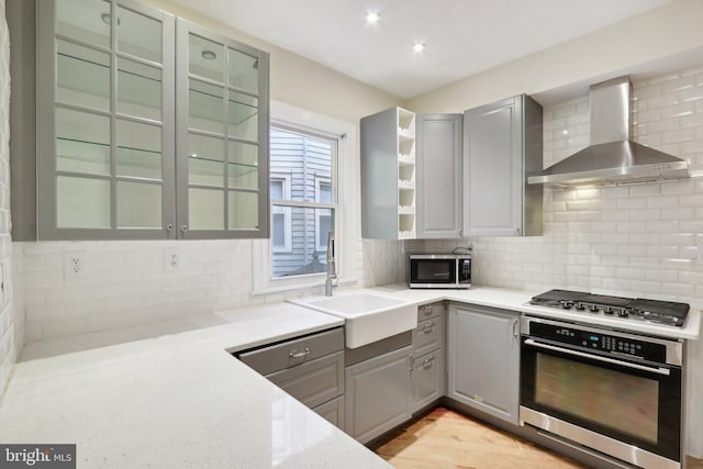 kitchen with wall chimney range hood, light stone countertops, appliances with stainless steel finishes, sink, and decorative backsplash