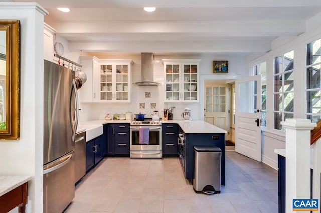 kitchen with decorative backsplash, wall chimney range hood, stainless steel appliances, blue cabinetry, and white cabinets