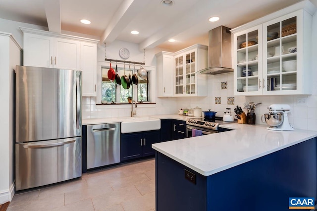 kitchen featuring wall chimney range hood, white cabinets, appliances with stainless steel finishes, beamed ceiling, and sink