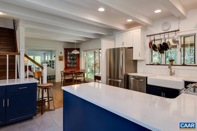 kitchen with appliances with stainless steel finishes, white cabinetry, beamed ceiling, and plenty of natural light