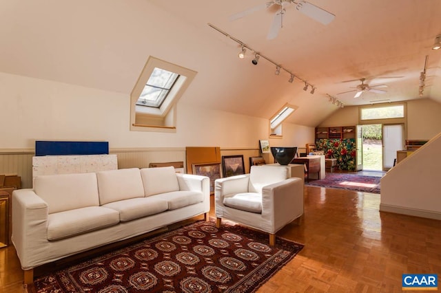 living room featuring parquet flooring, ceiling fan, vaulted ceiling with skylight, wooden walls, and track lighting