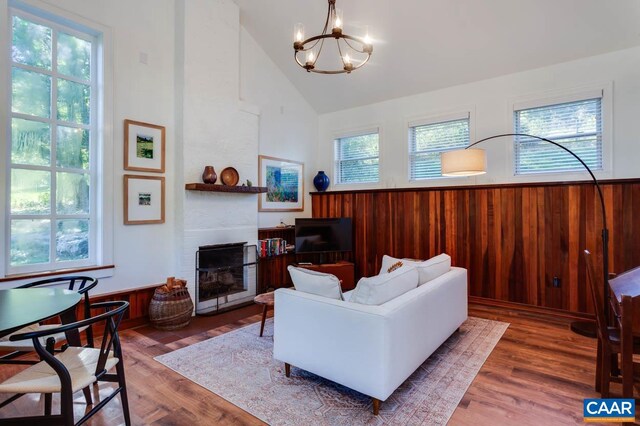 living room featuring dark hardwood / wood-style floors, wooden walls, a large fireplace, a notable chandelier, and high vaulted ceiling