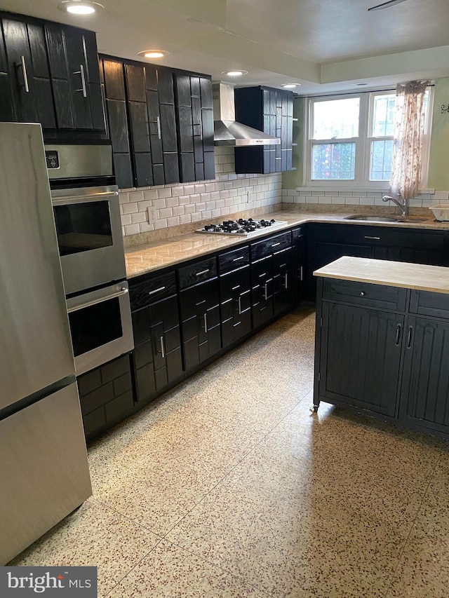 kitchen with appliances with stainless steel finishes, wall chimney exhaust hood, decorative backsplash, and sink