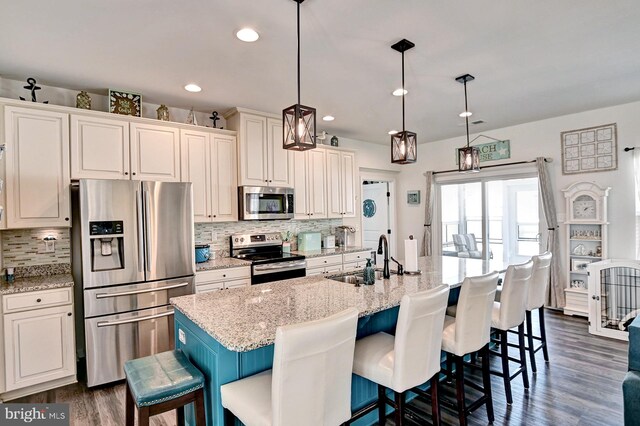 kitchen featuring a breakfast bar area, appliances with stainless steel finishes, light stone counters, and an island with sink