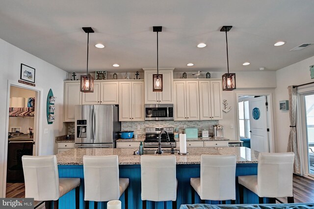 kitchen with a kitchen bar, stainless steel appliances, pendant lighting, light stone counters, and a center island with sink