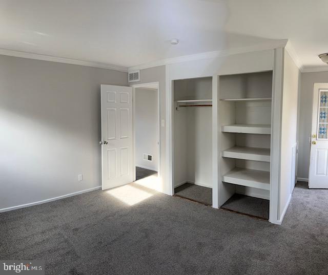 unfurnished bedroom featuring dark carpet, ornamental molding, and a closet