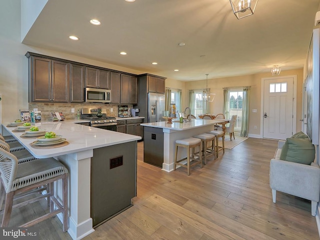 kitchen featuring stainless steel appliances, decorative light fixtures, a breakfast bar, kitchen peninsula, and light hardwood / wood-style flooring