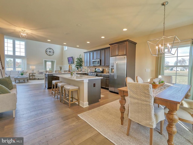 kitchen with appliances with stainless steel finishes, a kitchen bar, decorative light fixtures, an island with sink, and light hardwood / wood-style flooring