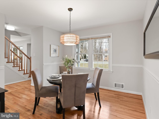 dining area with stairs, wood finished floors, visible vents, and baseboards