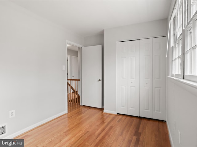 unfurnished bedroom featuring a closet, visible vents, baseboards, and wood finished floors