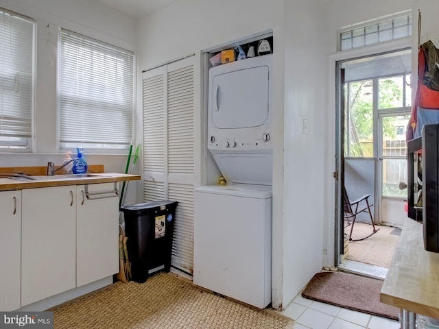 laundry area with stacked washer / drying machine, light tile patterned flooring, and sink