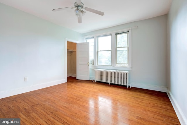 unfurnished bedroom with a closet, radiator, a spacious closet, light hardwood / wood-style floors, and ceiling fan