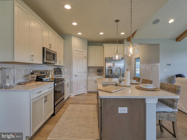 kitchen with stainless steel appliances, a center island with sink, sink, a kitchen bar, and white cabinets