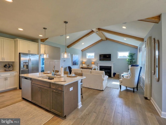 kitchen featuring appliances with stainless steel finishes, light wood-type flooring, an island with sink, pendant lighting, and lofted ceiling with beams