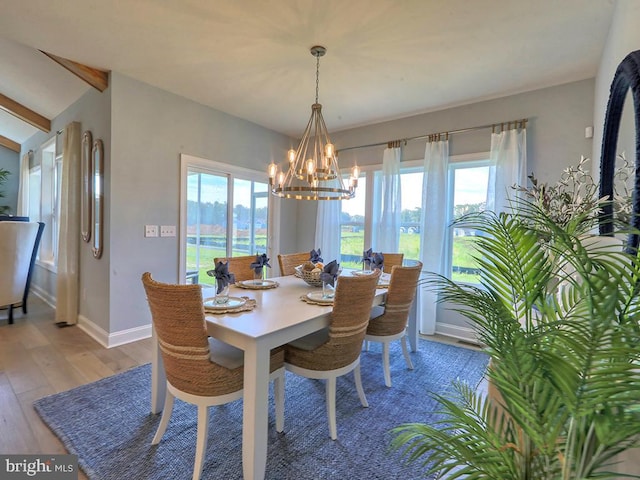 dining room featuring hardwood / wood-style floors, a healthy amount of sunlight, lofted ceiling, and a notable chandelier