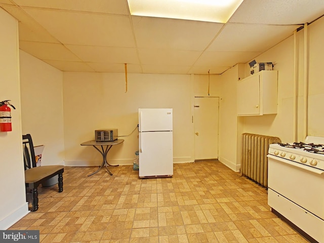 kitchen with radiator heating unit, white appliances, a drop ceiling, and white cabinets