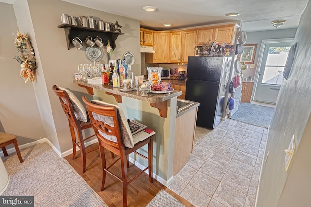 kitchen featuring light brown cabinets, kitchen peninsula, light tile patterned floors, a breakfast bar, and black refrigerator