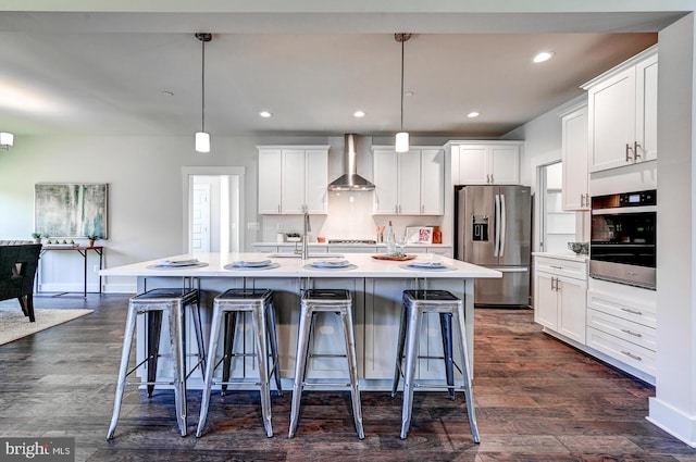 kitchen with appliances with stainless steel finishes, wall chimney range hood, decorative light fixtures, and an island with sink