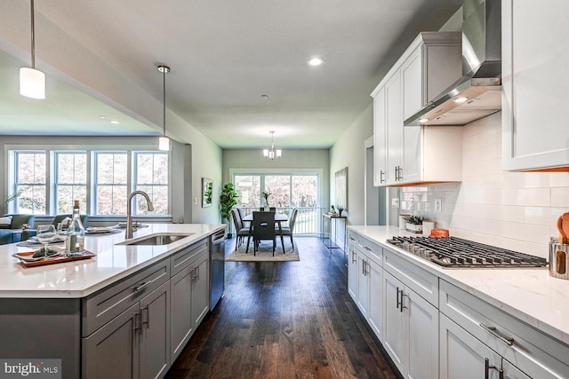 kitchen with wall chimney range hood, hanging light fixtures, dark hardwood / wood-style flooring, appliances with stainless steel finishes, and sink