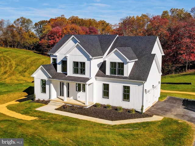 modern inspired farmhouse with a front lawn, covered porch, and a garage