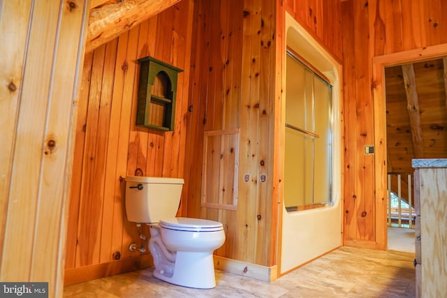 bathroom with combined bath / shower with glass door, toilet, and wood walls