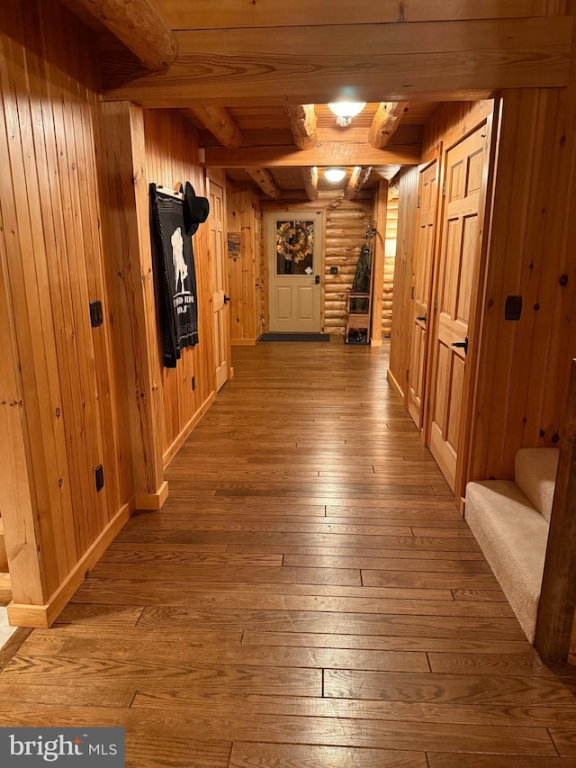 hall featuring beam ceiling, wooden walls, and wood-type flooring