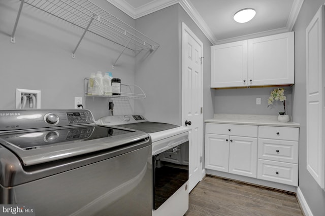 washroom with ornamental molding, washer and clothes dryer, wood-type flooring, and cabinets