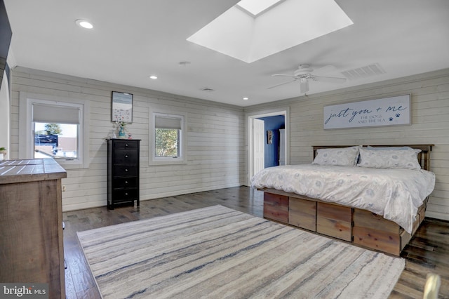 bedroom featuring wood walls, dark wood-type flooring, a skylight, and ceiling fan