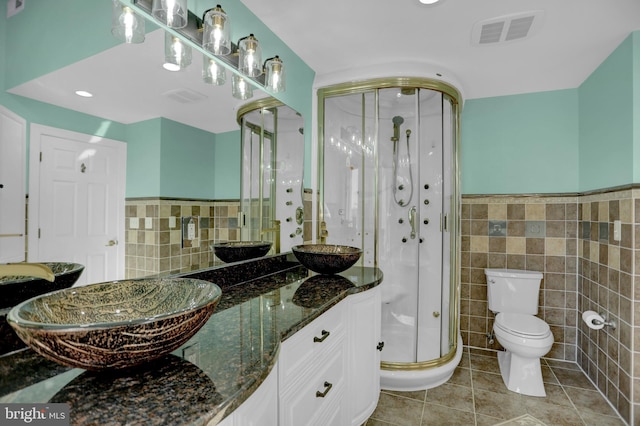 bathroom with toilet, walk in shower, tile walls, vanity, and tile patterned flooring