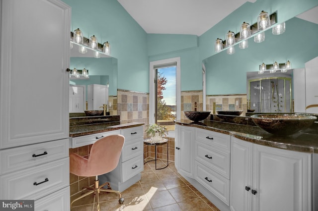 bathroom with a shower with door, lofted ceiling, decorative backsplash, tile patterned flooring, and vanity