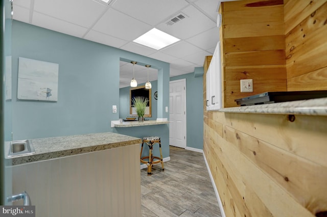 interior space with a paneled ceiling, kitchen peninsula, pendant lighting, and hardwood / wood-style floors