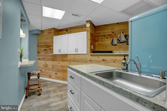 kitchen with a drop ceiling, light hardwood / wood-style flooring, wood walls, and pendant lighting