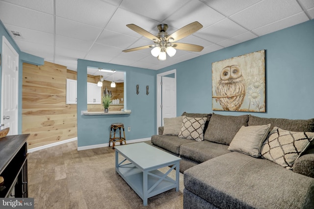 living room featuring a drop ceiling, wood walls, hardwood / wood-style floors, and ceiling fan