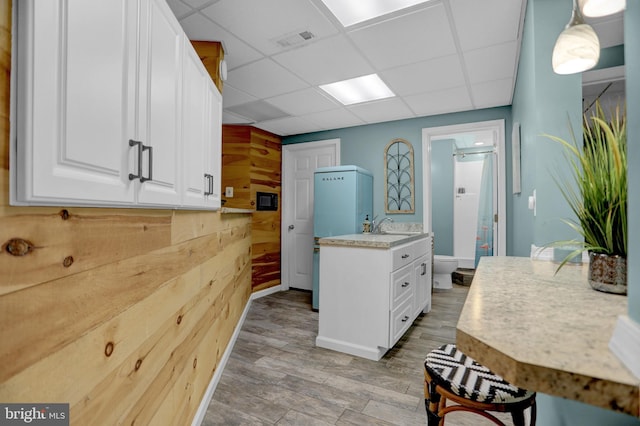 kitchen featuring hanging light fixtures, white cabinetry, light hardwood / wood-style floors, a paneled ceiling, and wooden walls