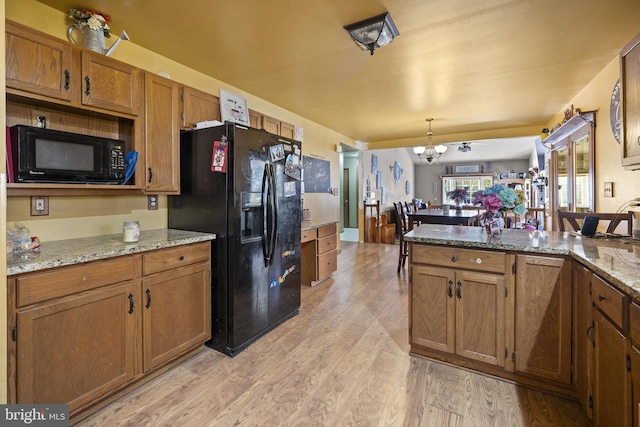 kitchen featuring black appliances, light stone countertops, light wood-type flooring, decorative light fixtures, and a chandelier