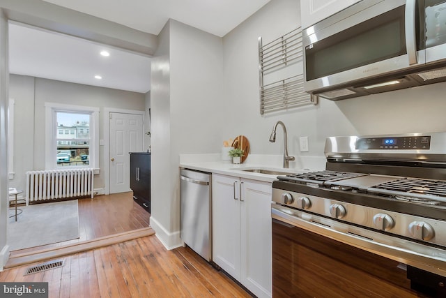 kitchen with white cabinets, sink, appliances with stainless steel finishes, light hardwood / wood-style floors, and radiator heating unit