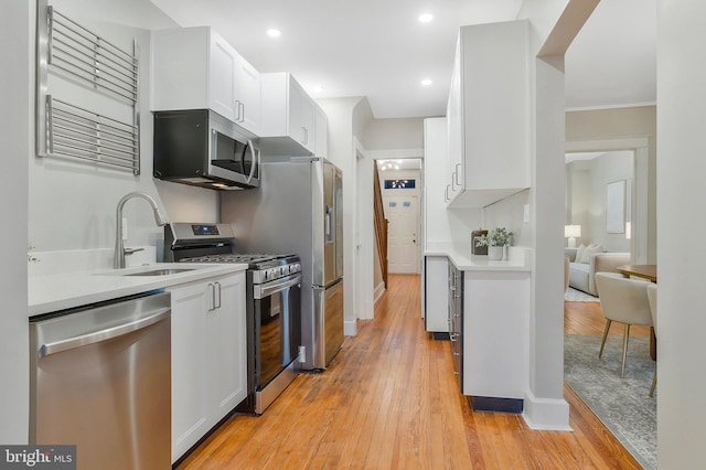 kitchen with sink, white cabinets, light wood-type flooring, and appliances with stainless steel finishes