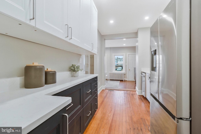 kitchen with white cabinets, light wood-type flooring, stainless steel appliances, and radiator