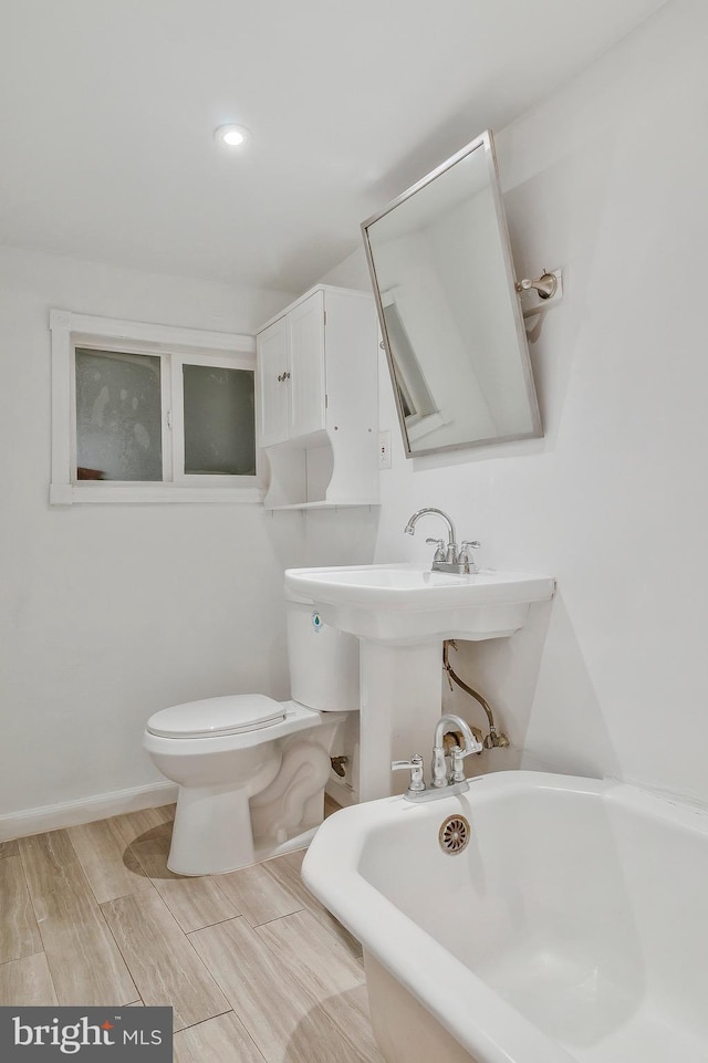 bathroom with a tub to relax in, toilet, and hardwood / wood-style flooring