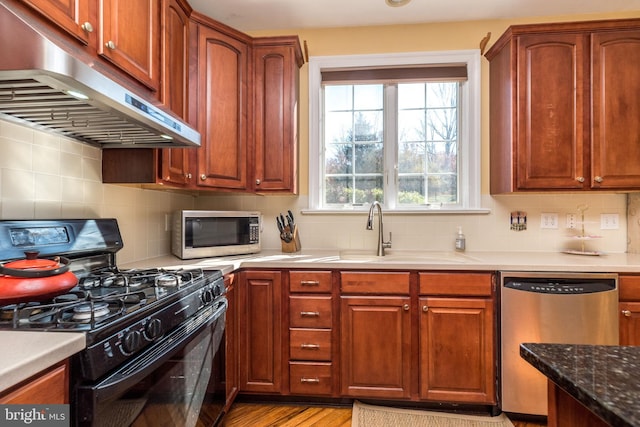 kitchen featuring decorative backsplash, appliances with stainless steel finishes, light wood-type flooring, dark stone counters, and sink